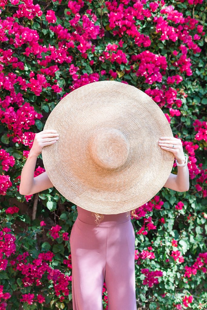 Women holding hat and focusing on her ideal client as it covers her face in front of Bougainvillea 